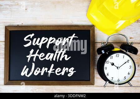 Support Health Workers text written on blackboard with safety helmet and alarm clock on wooden background Stock Photo