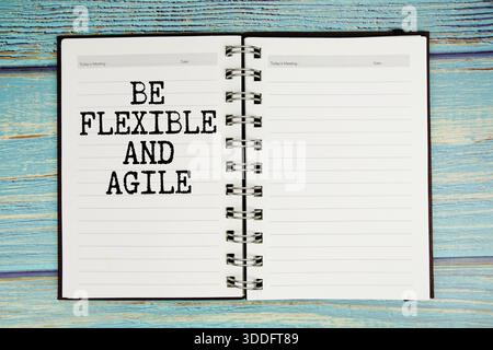 open spiral notebook on a blue wooden table with the words "Be Flexible And Agile" Stock Photo