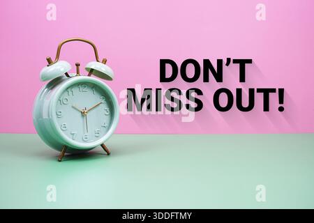 Black alarm clock on a pastel green and pink background with the text "Don't miss out" Stock Photo