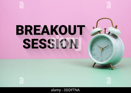 Black alarm clock on a pastel green and pink background with the text "Breakout session" Stock Photo