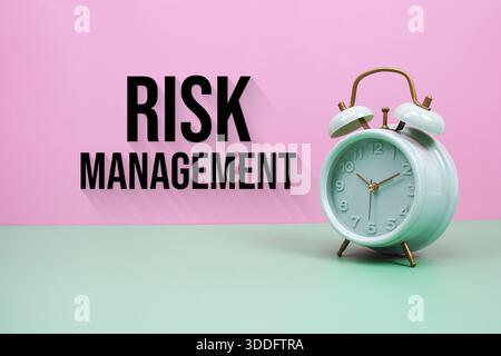 Black alarm clock on a pastel green and pink background with the text "Risk Management" Stock Photo