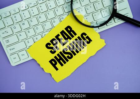 Yellow paper with text "Spear Phishing" and magnifying glass placed on a white keyboard Stock Photo