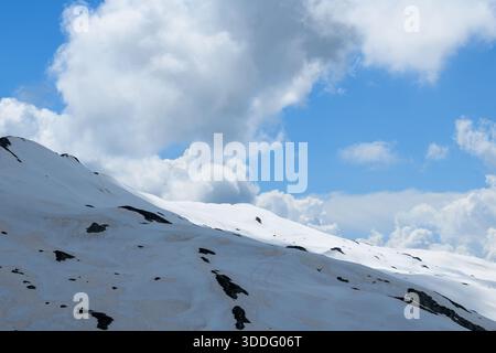 Undisturbed snow blankets the gentle slopes of Aiguillette des Houches, with dramatic cumulus clouds drifting across a vivid blue sky and subtle rock outcrops emerging from the white landscape. Stock Photo