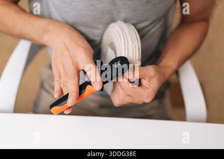 Person hands holding cable crimping tool, preparing white electrical wire for secure connection, performing precise task of installation or repair and Stock Photo
