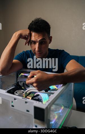 Vertical portrait of puzzled technician upgrading desktop computer by installing wi-fi module, focusing intently on task with thoughtful expression Stock Photo