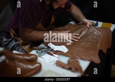 Leather artisan at work shaping brown leather with tools on a table for handmade craft Stock Photo