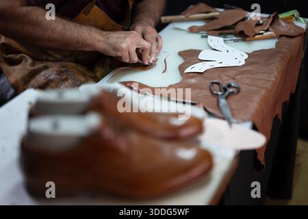 Leather craftsman at work shaping leather with tools and patterns on a workshop table Stock Photo