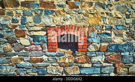 Abandoned Mine Stone Wall With Red Brick Archway and Sunlit Texture Stock Photo