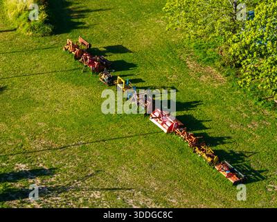 Various vintage farm implements and equipment are arranged in a neat, extended row across a vibrant green field, casting long shadows. Stock Photo