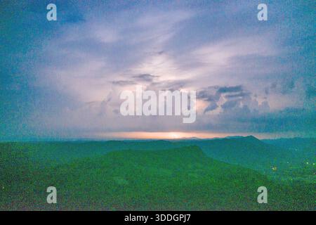 A single bolt of lightning illuminates the horizon under expansive thunderclouds, with distant hills silhouetted against a moody blue twilight sky. The scene captures dramatic cloud formations, subtle gradients, and the atmospheric tension of an approaching storm. Stock Photo