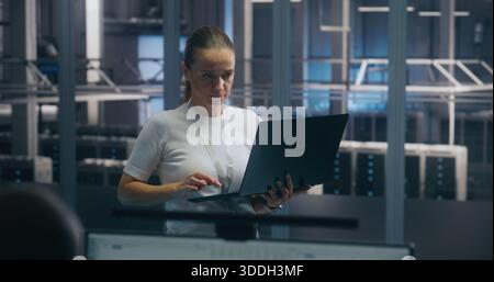 Experienced Female Engineer Uses Portable PC Run Diagnostics Performance Metrics in Bright, Secure Data Center Environment. Concept On Site Troubleshooting, IT Expertise, and Infrastructure Integrity. Stock Photo