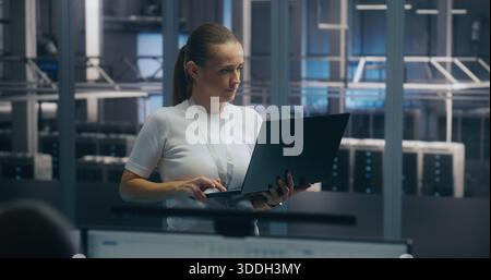 Experienced Female Engineer Uses Portable PC Run Diagnostics Performance Metrics in Bright, Secure Data Center Environment. Concept On Site Troubleshooting, IT Expertise, and Infrastructure Integrity. Stock Photo