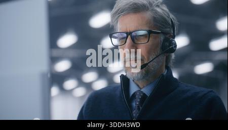 Close Up of Serious, Grey Haired Male Senior Engineer Talking on Professional Headset in Data Center. Concept of Remote Technical Support, Client Communication, and Cloud Solutions. Portrait. Stock Photo