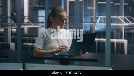 Experienced Female Engineer Uses Portable PC Run Diagnostics Performance Metrics in Bright, Secure Data Center Environment. Concept On Site Troubleshooting, IT Expertise, and Infrastructure Integrity. Stock Photo