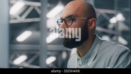 Close Up of Dedicated Engineer Oversees Digital Infrastructure From Workstation. Blue Lit, High Security Data Center Environment Visible in Soft Focus. Professional Monitoring and Technical Expertise. Stock Photo