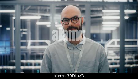 Bearded Male IT Engineer With Glasses, Smiling Confidently While Adjusting Eyewear. Man Standing in Secure, High Tech Environment of Data Center. Concept Expertise and Professional Demeanor. Portrait. Stock Photo