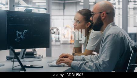 Focused Specialists Monitoring Factory Automation Work. Male and Female Technical Specialist Monitoring Real Time Factory Automation on Dual Screen Workstation. Process Control, Technical Oversight. Stock Photo