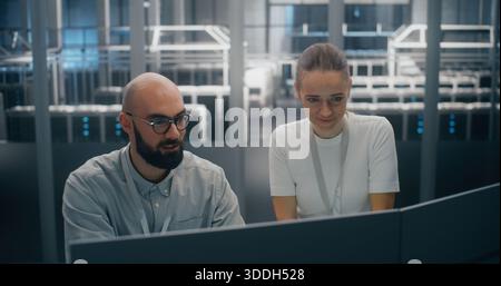 Two Focused IT Specialists Jointly Analyzing System Logs or Security Data on Screen. Secure and High Tech Setting of Server Hall Visible in Background. Critical Data Analysis and IT Security Protocol. Stock Photo