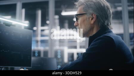 Mature Manager in Formal Attire and Glasses Using Workstation in High Security Modern Data Center. Working in Corporate IT Environment. Concept of Corporate Control and Serious IT Responsibilities. Stock Photo