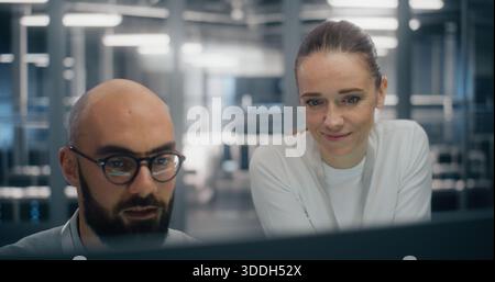 Team Consulting Over Console in Control Room. Digital infrastructure experts consulting over workstation console, deeply engaged in technical discussion. Concept of enterprise level system management. Stock Photo