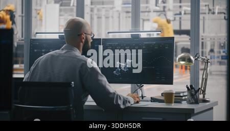 Two Professionals Working in Modern Industrial Control Room, With One Engineer Focused on Dual Monitors Displaying Automation Metrics. Data Analysis, and Robotics Management in Smart Manufacturing. Stock Photo