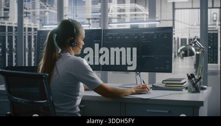 Female Technical Specialist Communicates Via Headset While Tracking Metrics and Graphs Data on Multi Screen Setup in Data Center. Control and Support, Expert Consultation, and Complex Problem Solving. Stock Photo