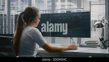 Young Female Professional Manages Large Servers Operations From Modern Workstation. Woman Wears Headset For Active Communication. Technological Innovation, Diverse Workforce and Innovative Workplace. Stock Photo