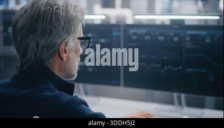 Mature Man Working in Large Scale Data Center. Experienced Engineer Typing and Performing System Diagnostics on Multiple Monitors in Tech Facility. Concept High Level Control, Focused Troubleshooting. Stock Photo
