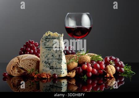 Gorgonzola cheese with ciabatta, walnuts, grapes, and red wine. Tradition Italian blue mold cheese with fruits and aromatic herbs on a black reflectiv Stock Photo