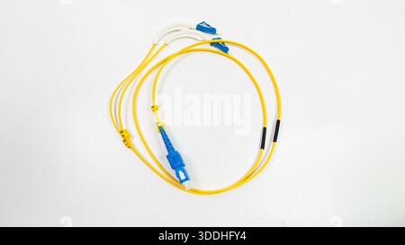 A yellow and blue cable is laying on a white surface. The cable is made of plastic and is connected to a device Stock Photo