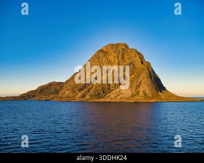 Golden winter light hits a rugged mountain island above calm blue water on the Norwegian coast, under a clear sky with ample copy space. Stock Photo