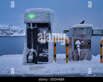 Bodo, Norway - Nov 17 2025: Snow-covered shore power hookup stations on the waterfront in Bodo, Norway, with a green status light and icy harbor backdrop on a cold winter day. Stock Photo