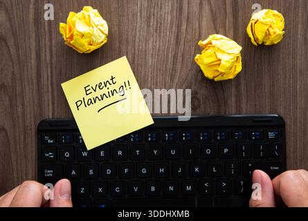 Person typing on a keyboard with event planning sticky note and crumpled paper Stock Photo