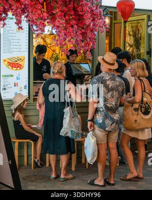 Sunset Town on Phu Quoc Island. December 23, 2025. People Ordering from a Vibrant Street Food Stall with Red Blossoms and Blue Plastic Chairs Stock Photo