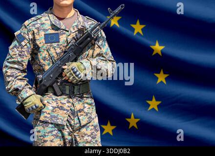 European union flag with soldier in military uniform holding assault rifle in front of it Stock Photo