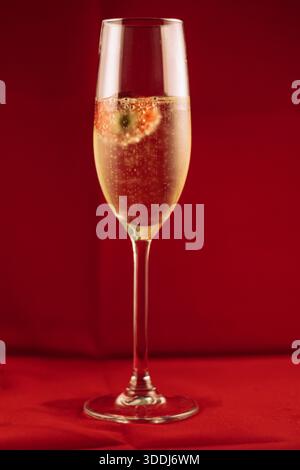 Elegant glass flute holding sparkling wine, releasing tiny bubbles, with a fresh strawberry floating inside. Romantic celebration concept Stock Photo