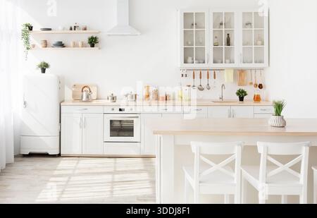 Light kitchen furniture after renovation. Kitchenware and plants on shelves, chairs and table in scandinavian style Stock Photo