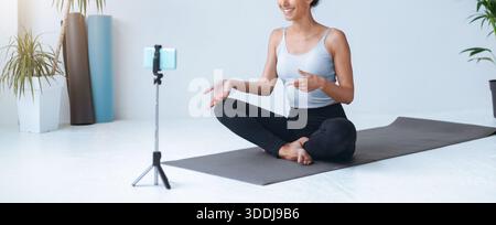 Yoga Instructor Leads Online Class on a Mat in a Bright Room With Plants and a Phone Camera Stock Photo