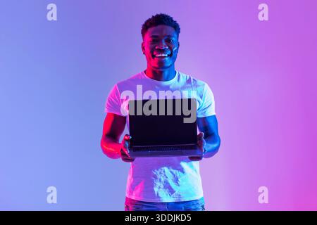 Handsome Young Black Man Holds Laptop With Blank Screen in Neon Light for Design Mockup Stock Photo
