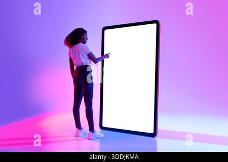 Millennial Black Woman Interacts With Large Tablet Screen in Neon Light Setting for App Design Stock Photo