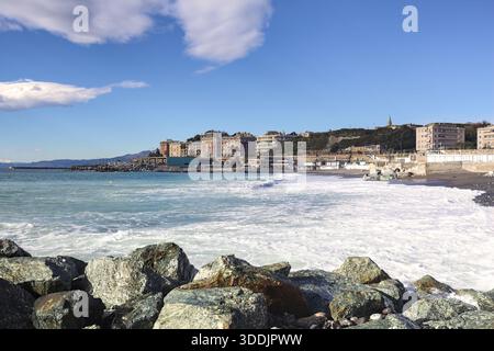 City buildings and a pebble beach by the sea on a sunny day with almost clear sky framed by a breakwater Stock Photo