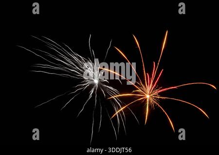 Silver and red fireworks explode in tandem over night, contrasting color streaks and sparkling tails create energetic synchronized display, urban fest Stock Photo
