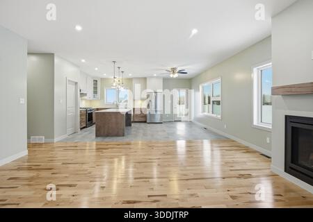 Large open living room with a fireplace and a kitchen. The room is clean and bright, with a lot of natural light coming in through the windows. The sp Stock Photo