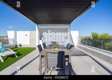 Stylish rooftop patio with dining area, built-in kitchen, pergola shade, and sunny views Stock Photo