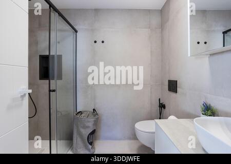 Minimalist bathroom featuring walk-in glass shower, laundry hamper, and sleek modern finishes Stock Photo
