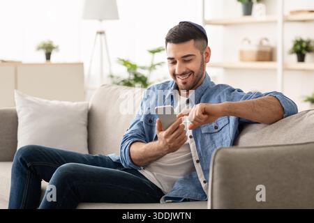 Smiling jew man using smart phone sitting on couch Stock Photo
