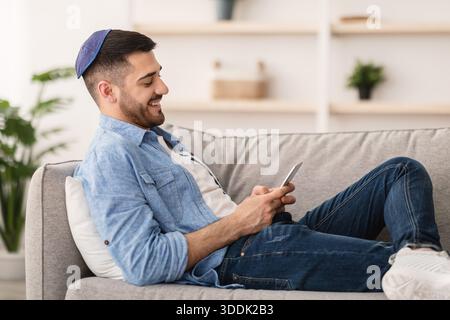 Smiling jew man using mobile phone sitting on couch Stock Photo