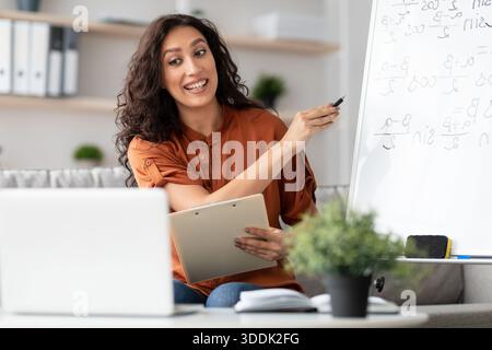 Female teacher explaining math to students using laptop holding clipboard Stock Photo