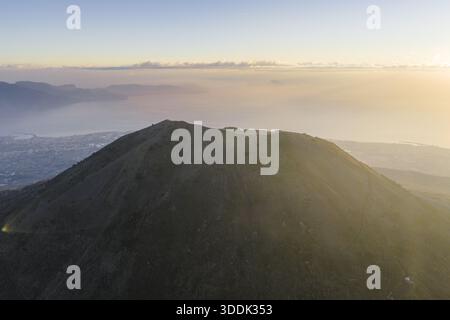Aerial view of the summit, bathed in the golden light of dawn, overlooking the distant city and the tranquil sea, Vesuvius National Park, Ercolano, Ca Stock Photo
