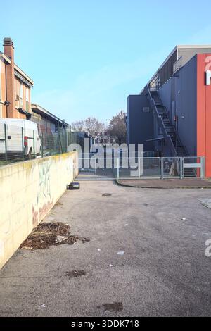 Back alley of a store, next to a concrete wall, behind a closed gate, full of scattered things, seen from above on a sunny day at sunset Stock Photo